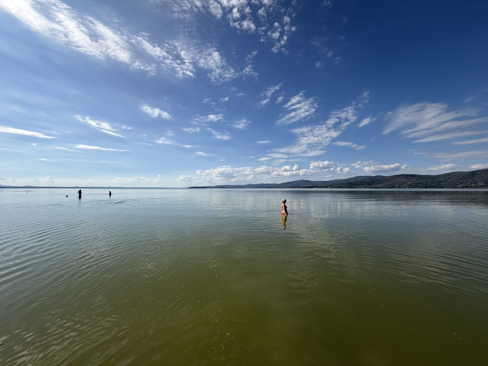Swimmers wading into the shallow water of Lake Trasimeno on a sunny afternoon