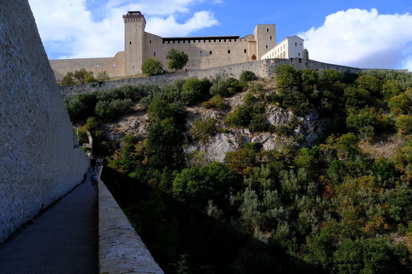 The walls of the Rocca Albornoziana above the wooded hillside, seen from the Giro della Rocca path